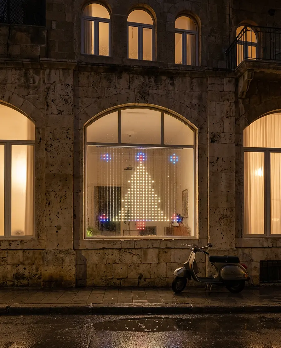 A Govee curtain light showing a Christmas tree in a window, seen from a rainy street